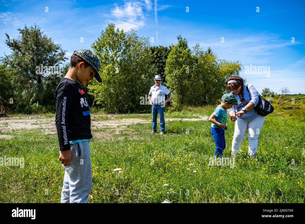 Adults and two children looking for something in green grass and weeds on a warm summer day by the Bernata street. Stock Photo