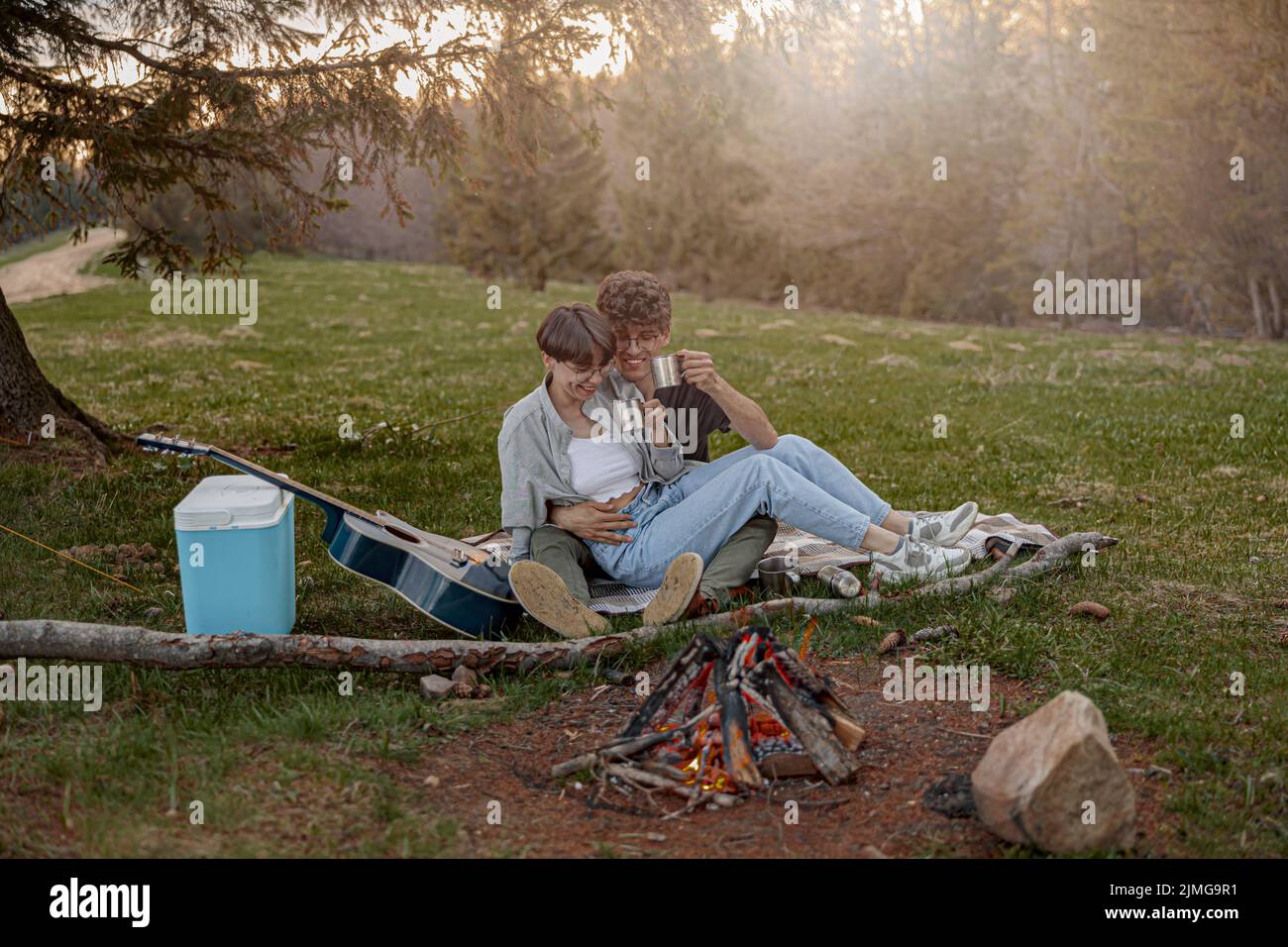 Happy young couple of tourists sitting in hug and laughing while having picnic. Weekend. Stock Photo
