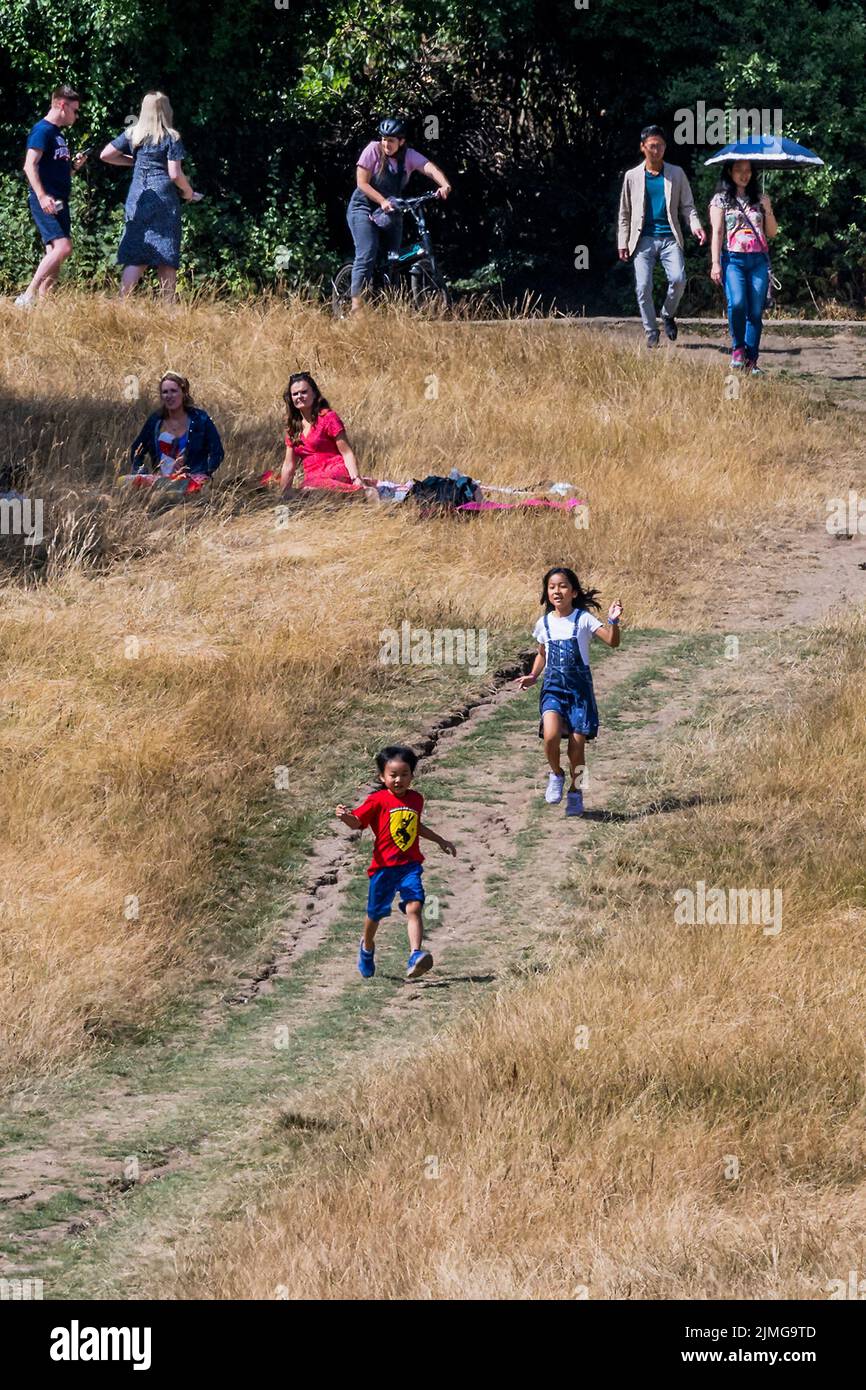 London, UK. 6th Aug, 2022. Children enjoy running down the dry path, which has a huge crack in it, amongst the yellow scorched grass of Parliament Hill - Hot weather continues the drought conditions on Hampstead Heath. Credit: Guy Bell/Alamy Live News Stock Photo