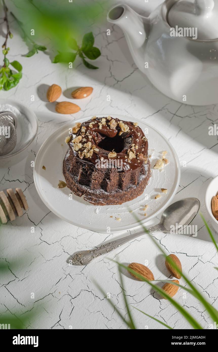 Brownie cake poured with chocolate and nuts on a white stand with hard light Stock Photo