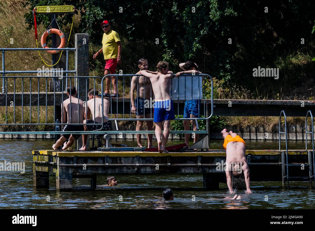 London, UK. 6th Aug, 2022. People dive in to the mens bathing pond to cool off, in stark contrast to the scorched grass on the hillside above - Hot weather continues the drought conditions on Hampstead Heath. Credit: Guy Bell/Alamy Live News Stock Photo