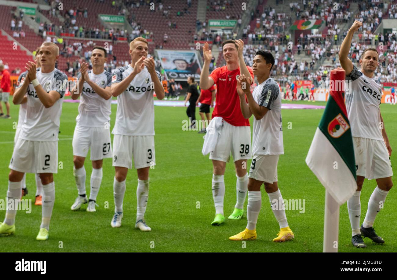 06 August 2022, Bavaria, Augsburg: Soccer, Bundesliga, FC Augsburg - SC Freiburg, Matchday 1, WWK Arena. Freiburg's Hugo Siquet (l-r), Nicolas Höfler, Philipp Lienhart, Michael Gregoritsch, Woo-Yeong Jeong and Christian Günter cheer in front of the fans after the victory. Photo: Stefan Puchner/dpa - IMPORTANT NOTE: In accordance with the requirements of the DFL Deutsche Fußball Liga and the DFB Deutscher Fußball-Bund, it is prohibited to use or have used photographs taken in the stadium and/or of the match in the form of sequence pictures and/or video-like photo series. Stock Photo