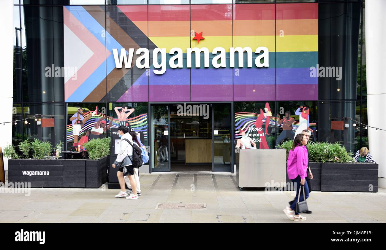 People walk past Wagamama restaurant, St Peter's Square, Manchester, United Kingdom, now with the Progress Flag on its frontage. Stock Photo