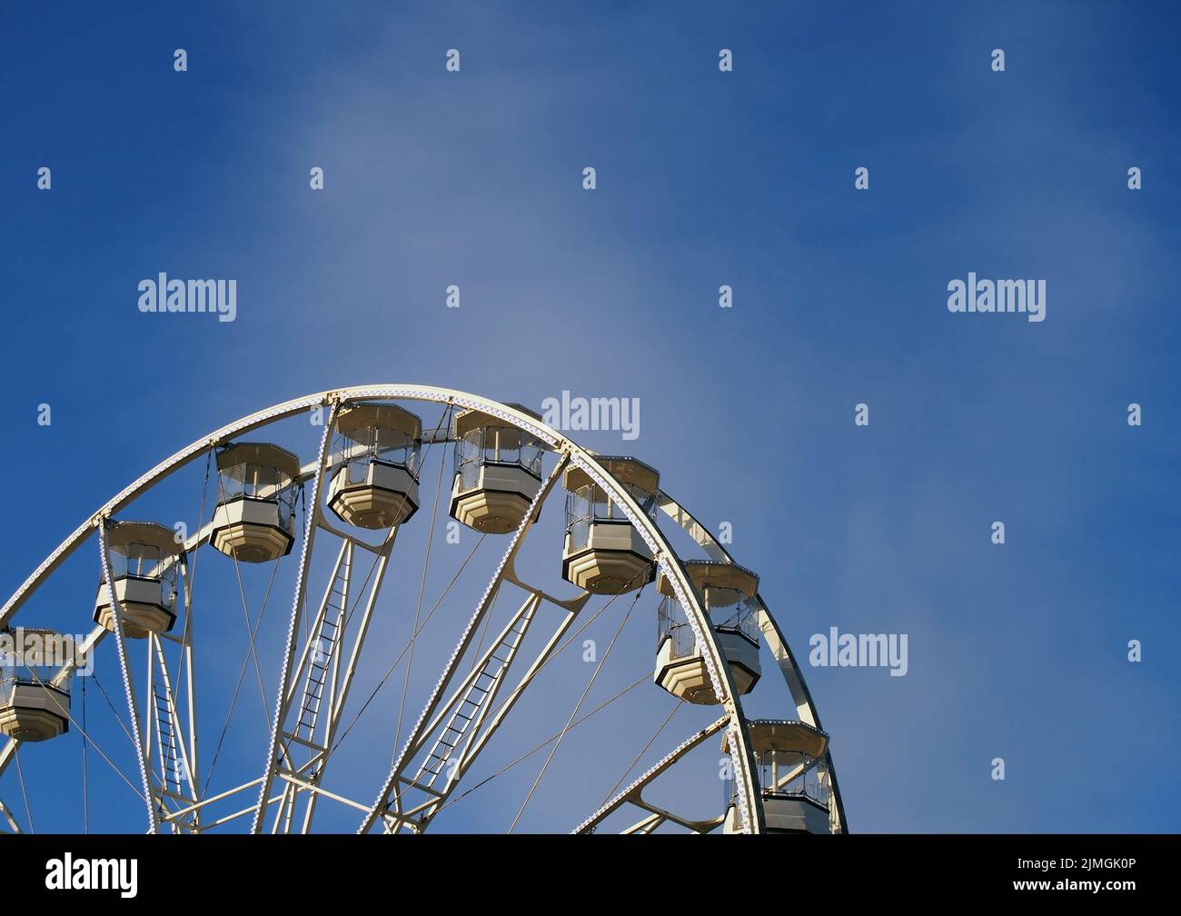 Close up of a white ferris wheel with enclosed gondola cars against a bright blue sky Stock Photo