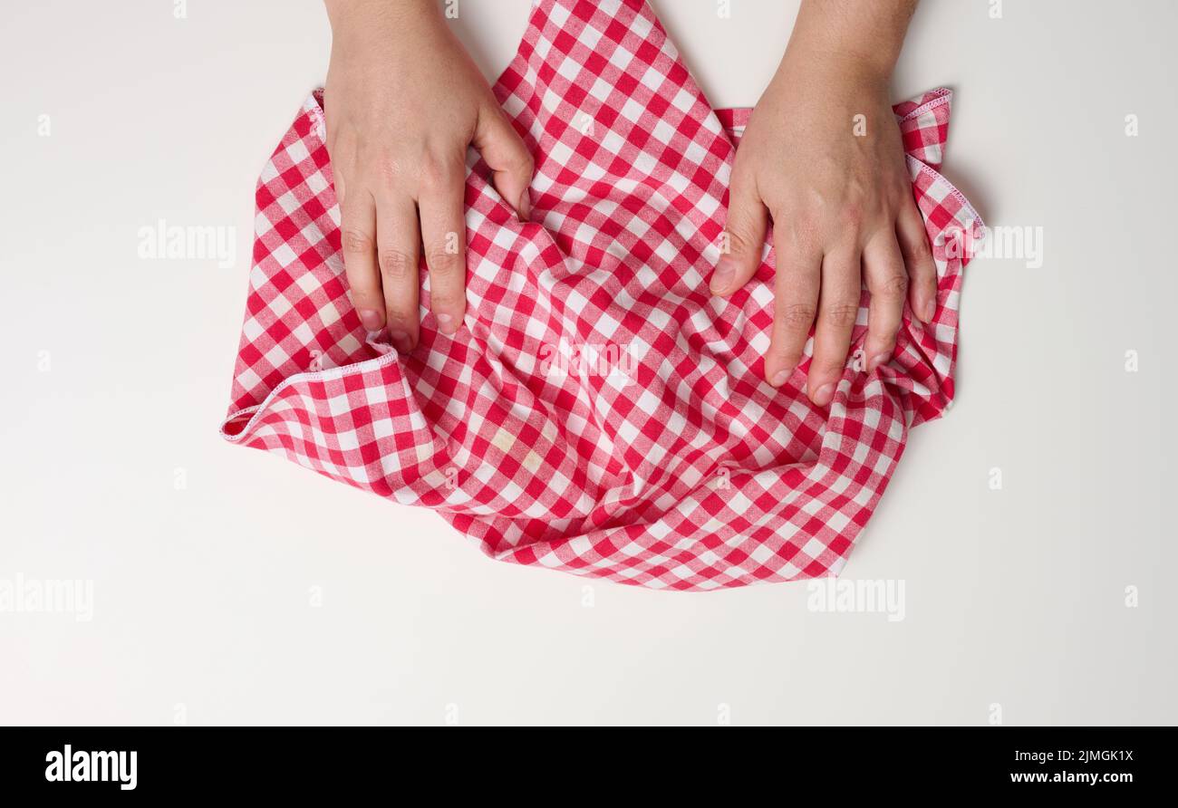 Two female hands holding a red kitchen napkin on a white table, top view Stock Photo