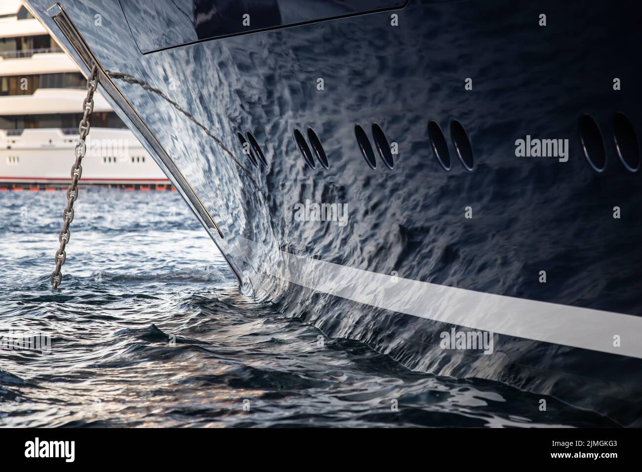 The mesmerizing reflection of the water on the glossy side of a huge yacht anchored, chrome details, chains and ropes to the mur Stock Photo