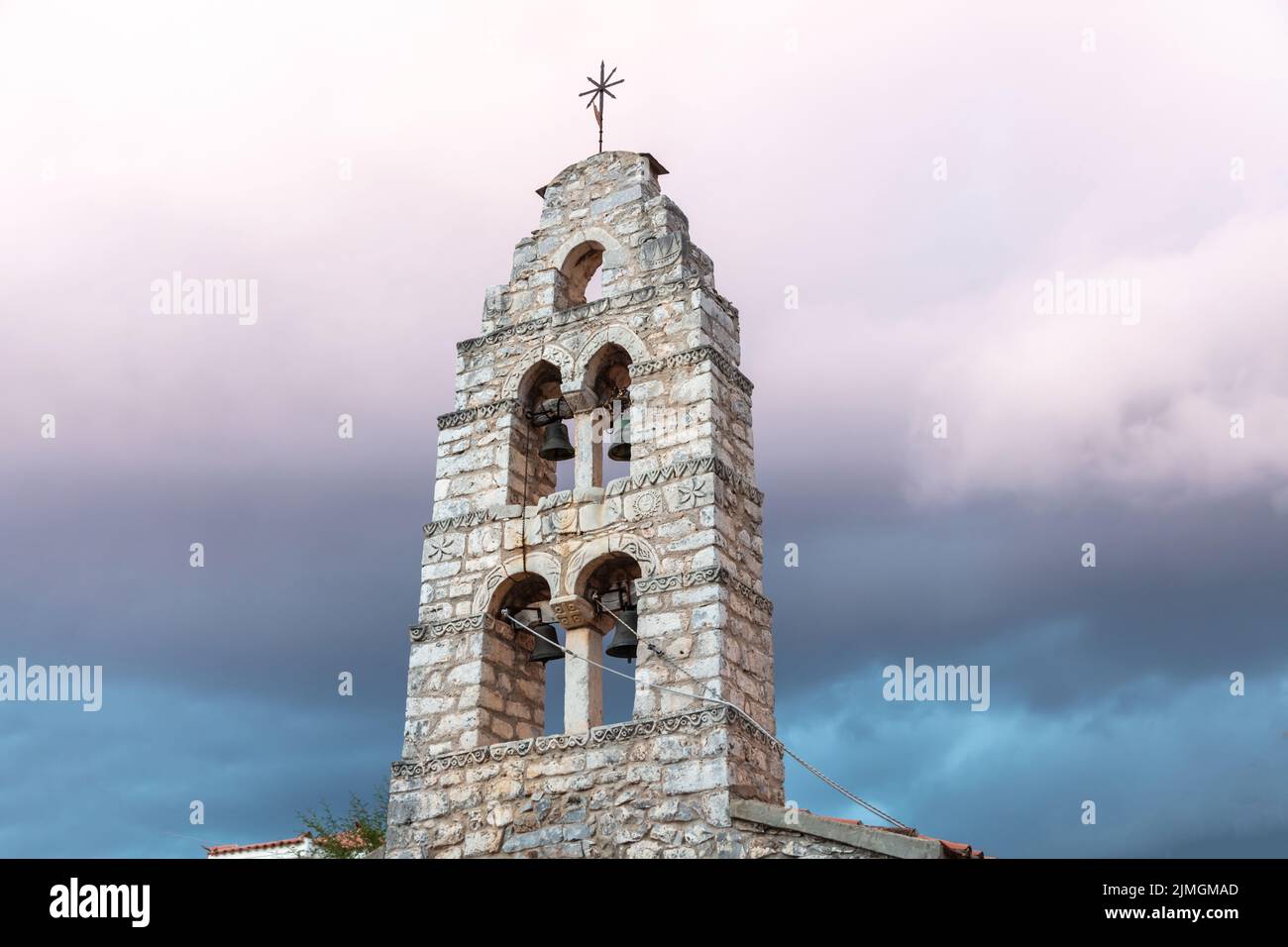 Belfry with four metal bronze bells at Mani Laconia, Peloponnese Greece. Under view of traditional stonewall bell tower with cross, cloudy sky backgro Stock Photo