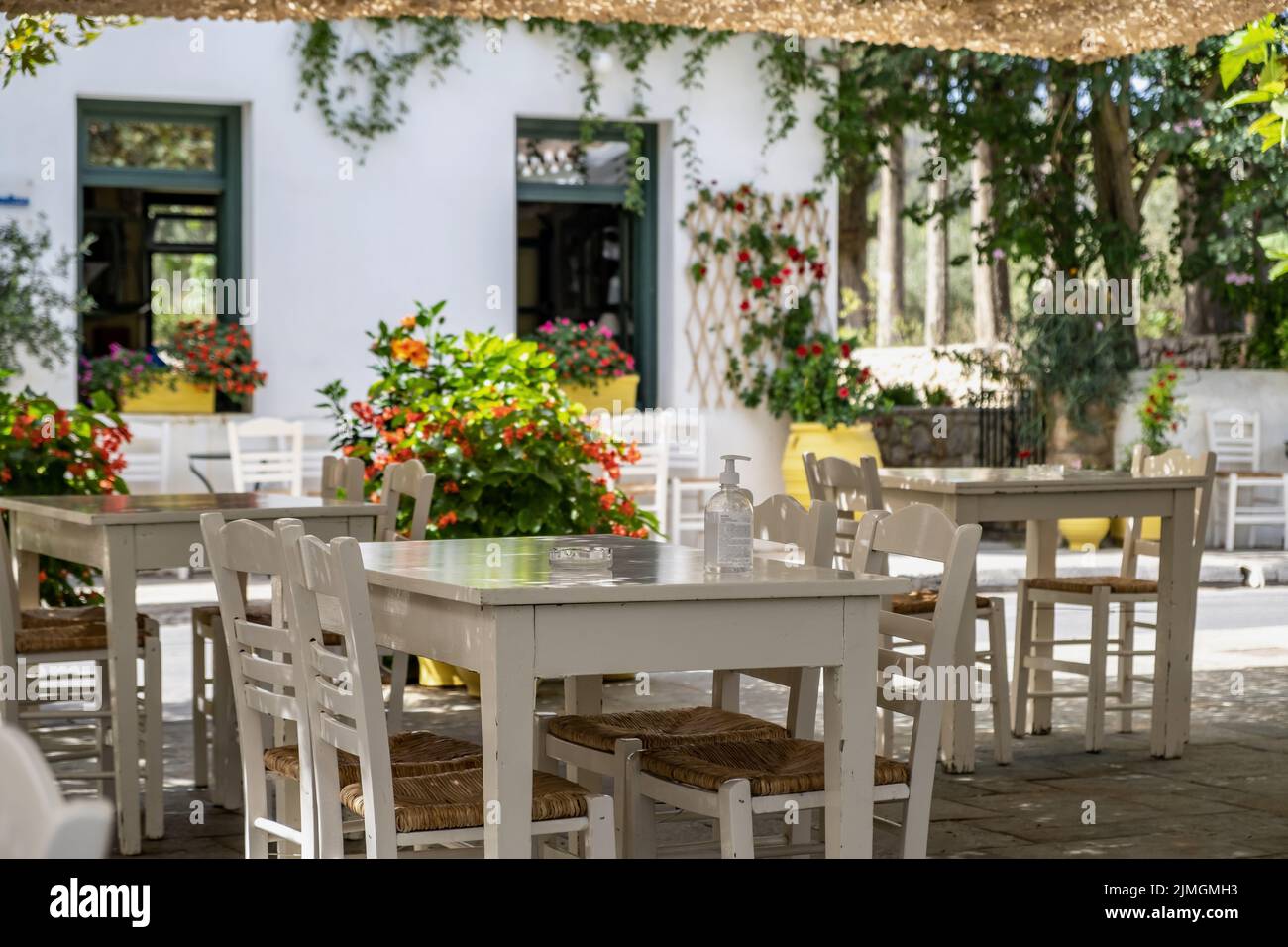 Greek outdoors tavern restaurant with empty white table and chair at Kithira Ionian islands Milopotamos village destination Greece. Pots with flowers Stock Photo