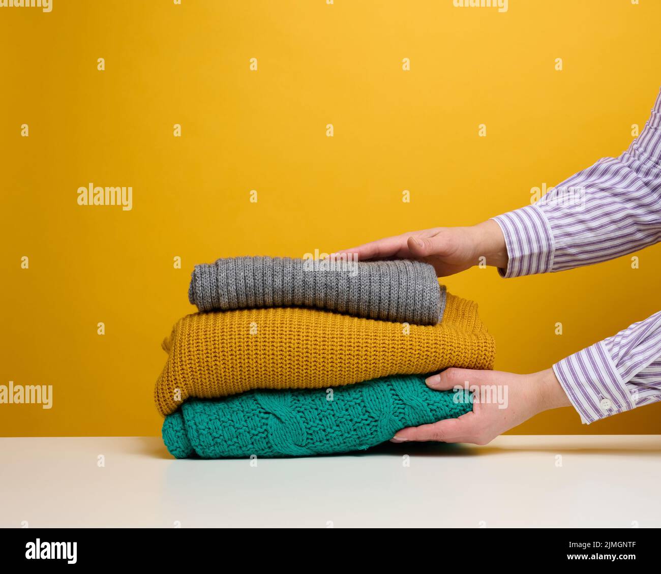 A woman holds a stack of washed folded things on a yellow background. Home routine work Stock Photo