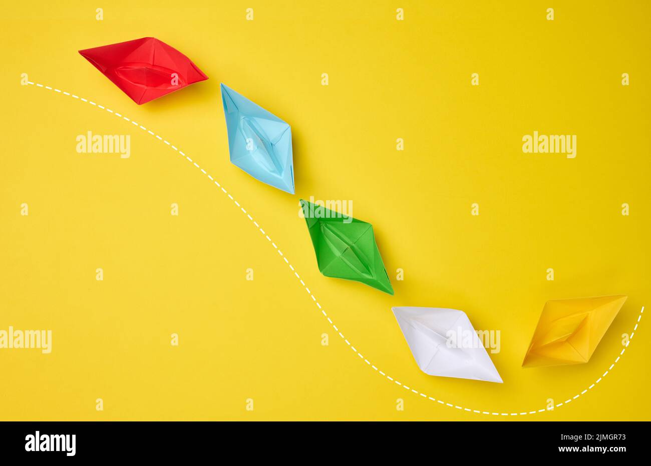 Multi-colored paper boats follow the leader on a yellow background. The concept of manipulation of the masses, the path for a st Stock Photo