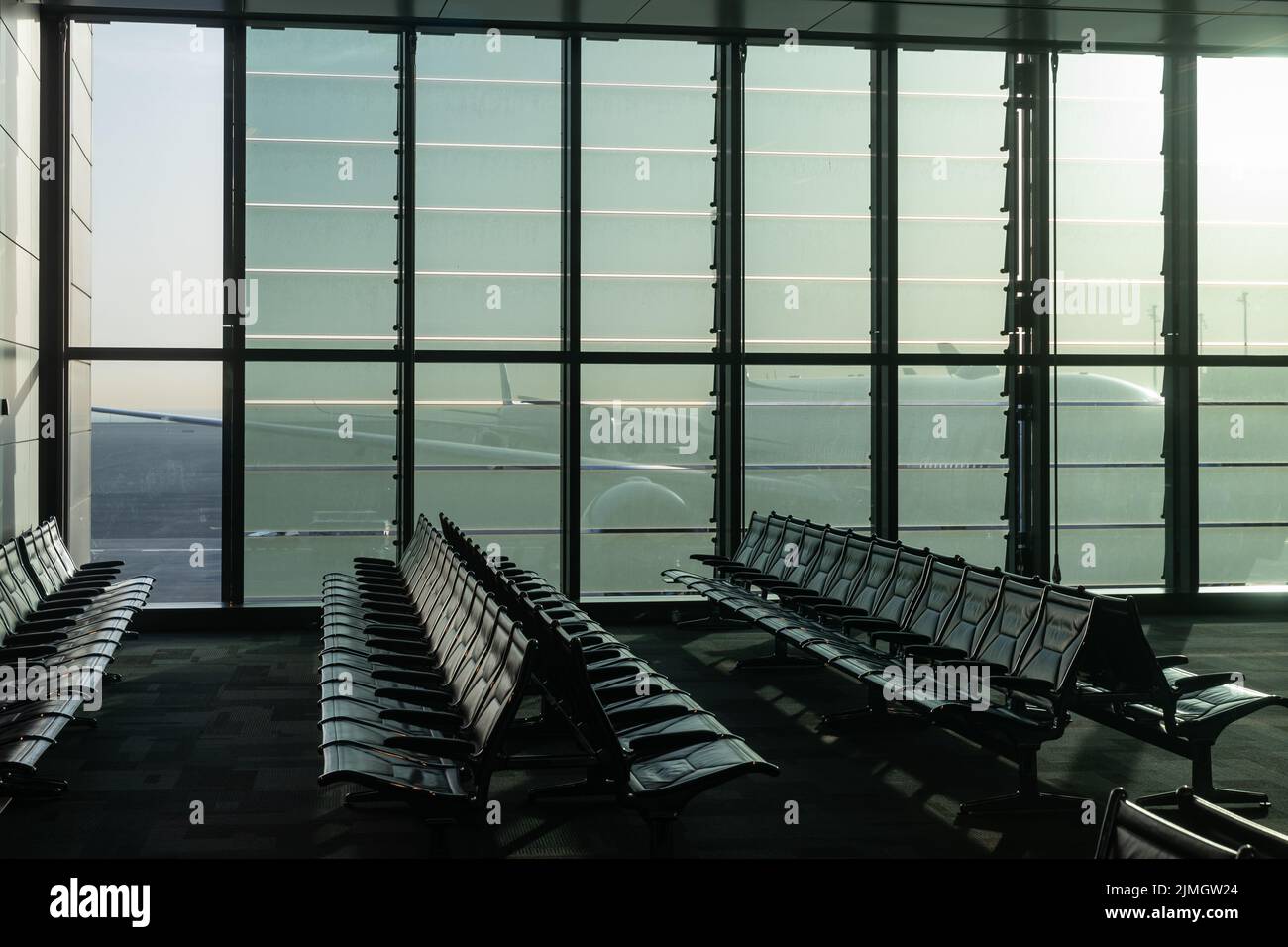 A deserted airport, empty benches by a panoramic window, a huge plane visible through the glass walls of an interchange hub in t Stock Photo