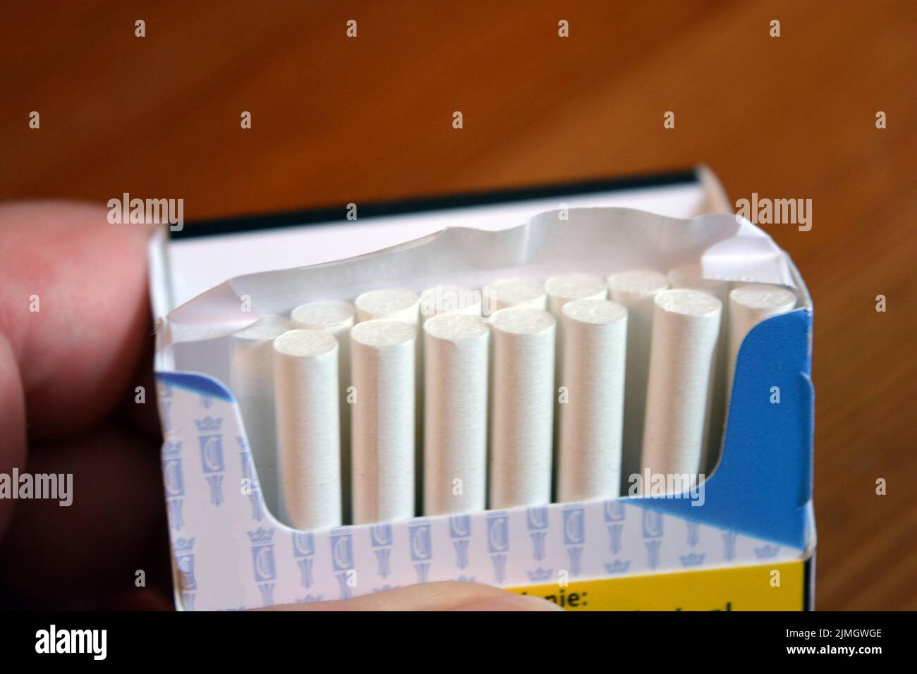 A pack of white thin cigarettes lying on a yellow wooden table. Stock Photo