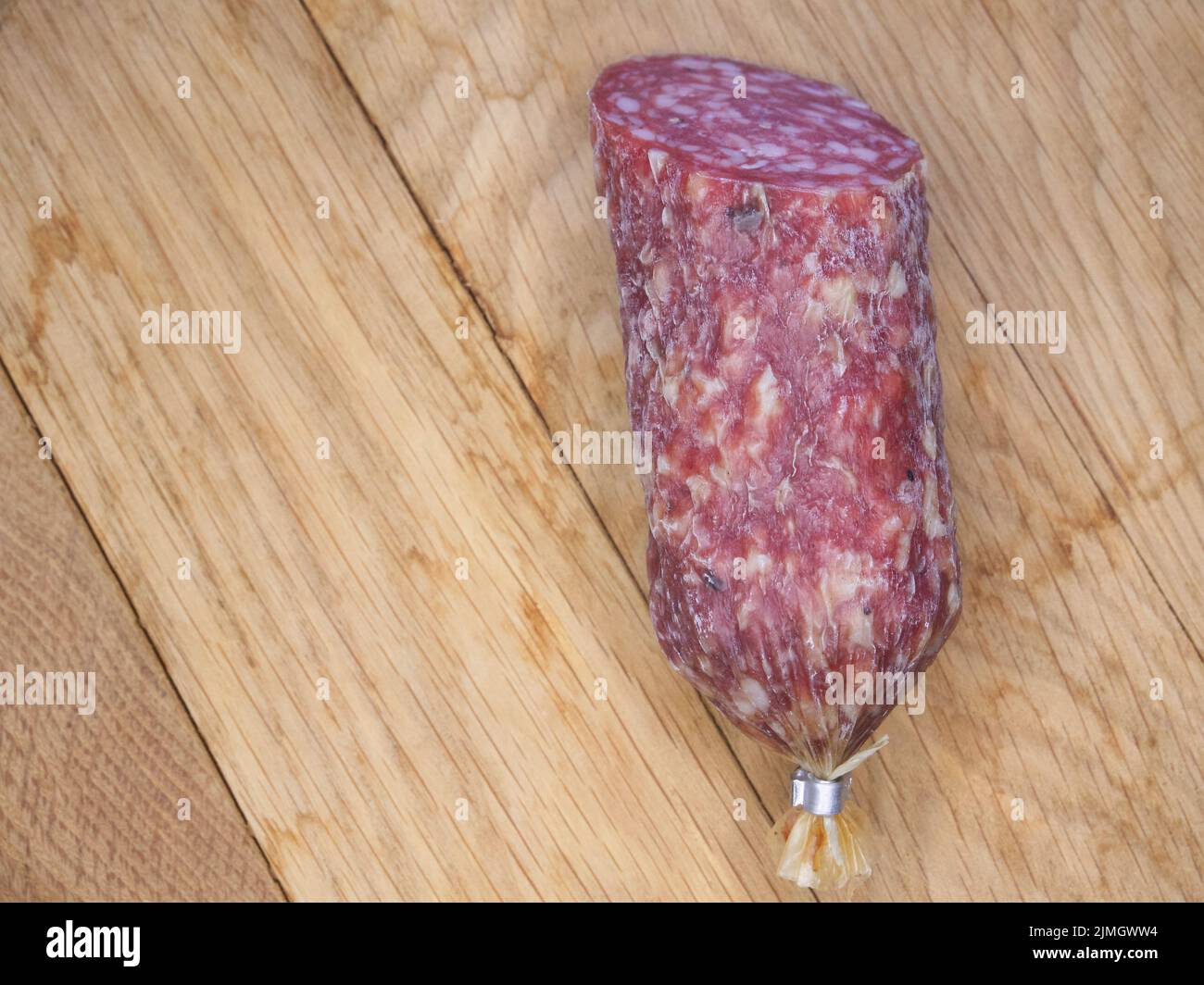 A large piece of smoked sausage on a wooden cutting board, close-up shot. Stock Photo