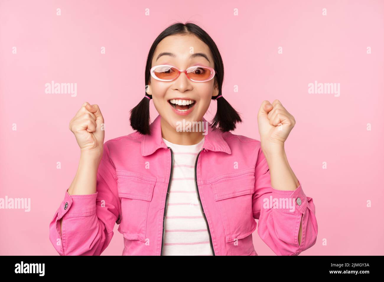 Portrait of excited japanese girl in sunglasses, celebrating, achieve