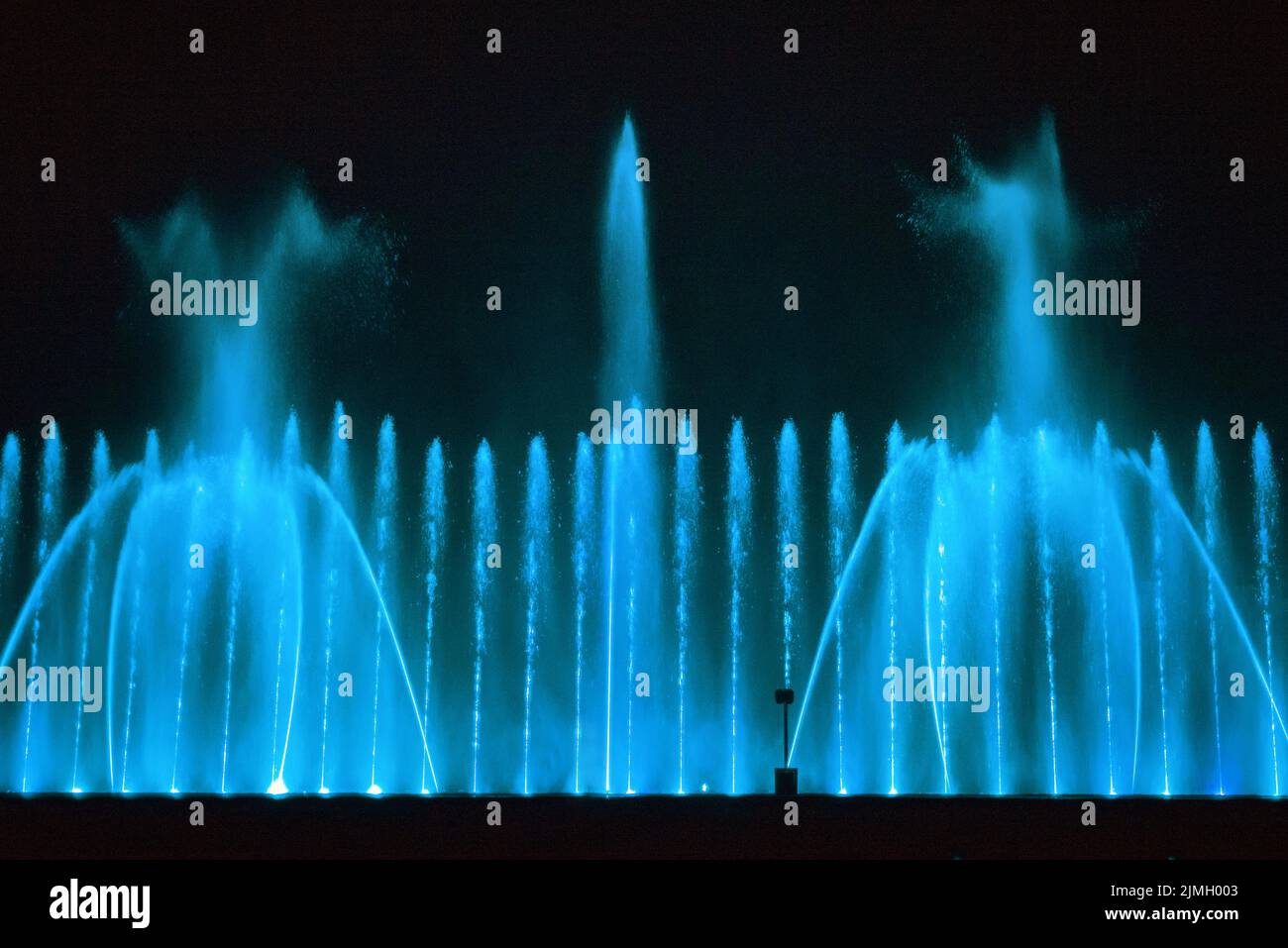 Beautiful fountain show. Large multi colored decorative dancing water jet led light fountain show at night. Dark background. Stock Photo