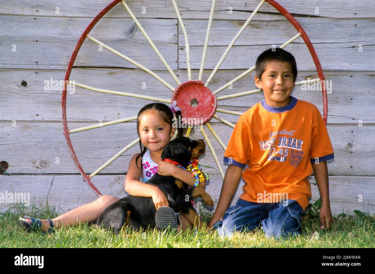 Two Native American children play with a puppy together. Fort Hall Idaho Stock Photo
