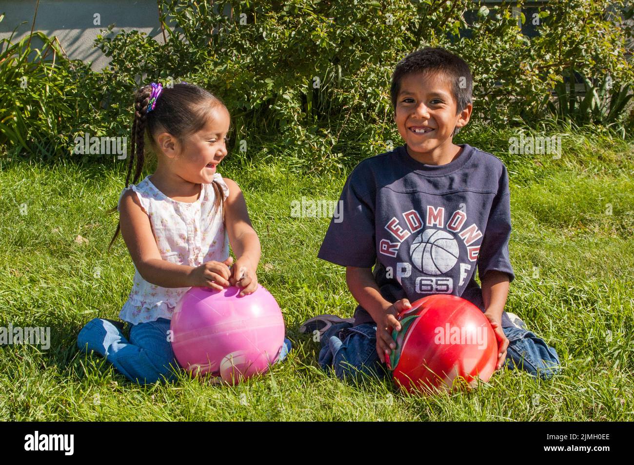 Two Native American children, sister and brother, play with large balls together outside. Stock Photo