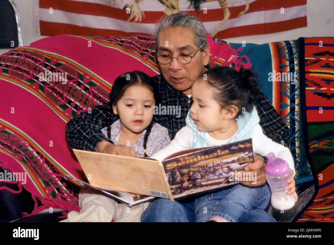 Native American family of Shoshone Bannock grandfather reading a story book to his two young grand-daughters Stock Photo