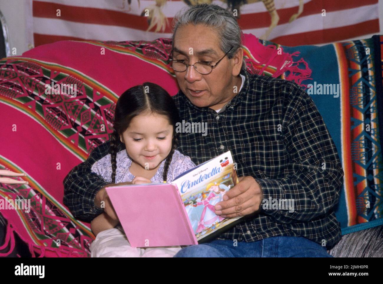 Native American family of a Shoshone Bannock grandfather reading a book about the story of Cinderella to his young grand-daughter Stock Photo