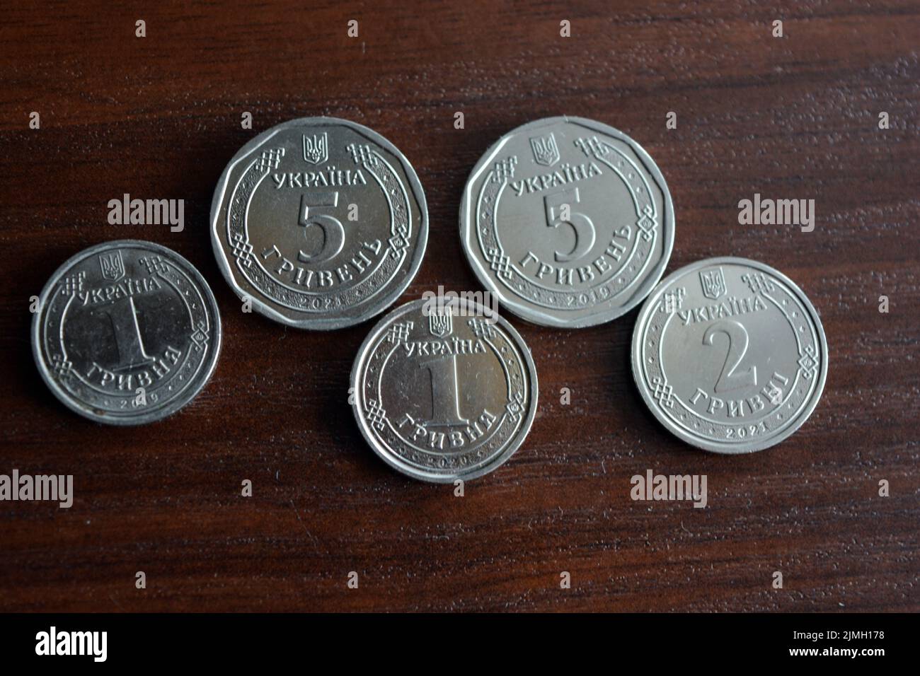 Ukrainian kopecks, small change in the amount of one 1, two 2, five 5 hryvnias are located on a dark brown table. Stock Photo