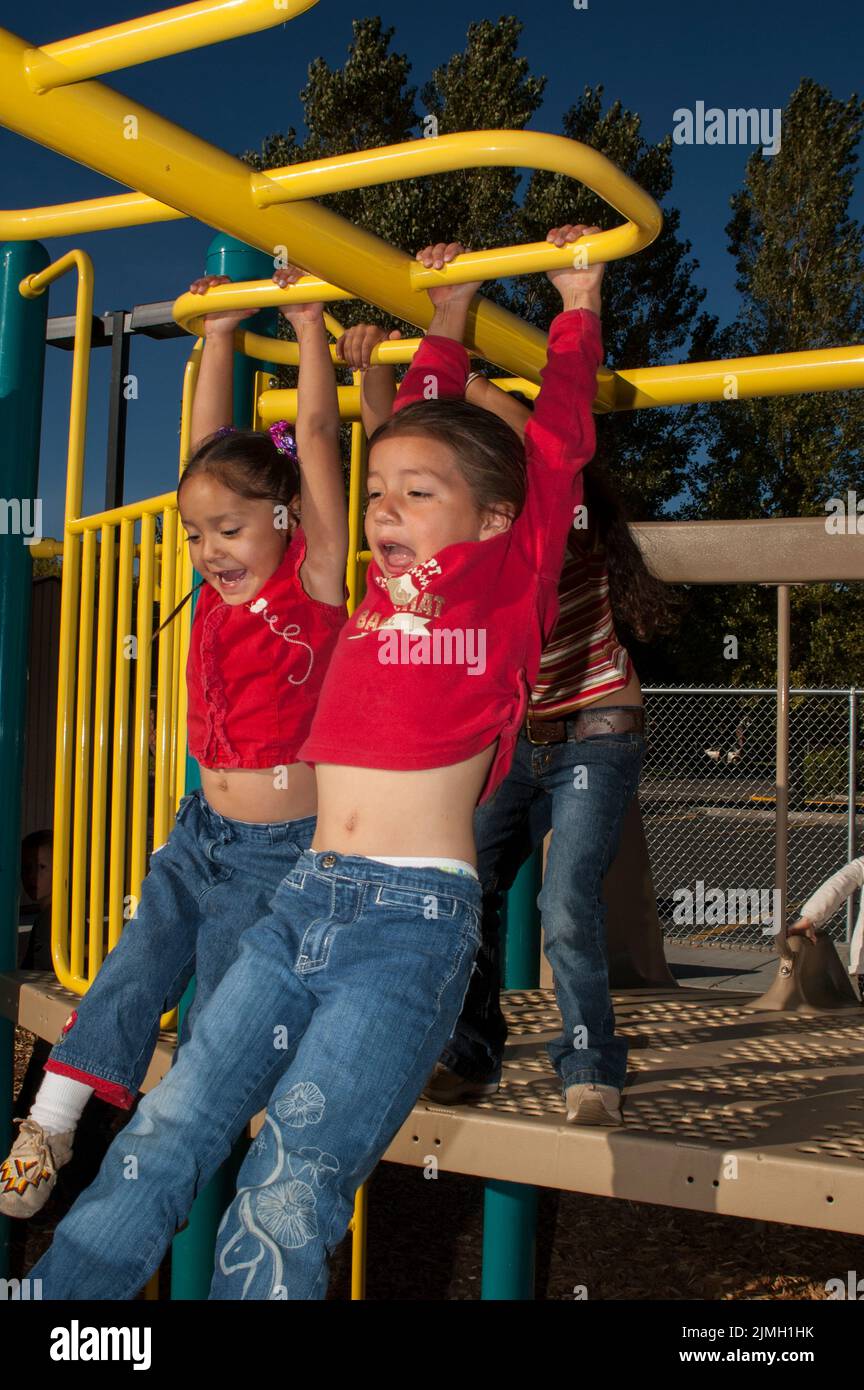 Three elementary age friends and cousins play on colorful monkey bars after school Stock Photo
