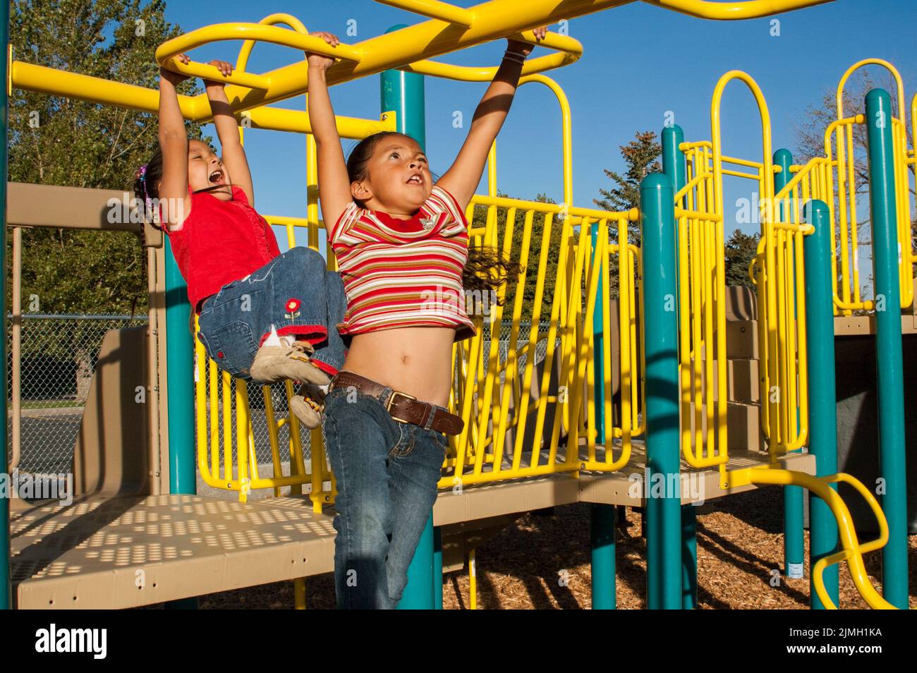 Two elementary age friends and cousins play on colorful monkey bars on their school playground