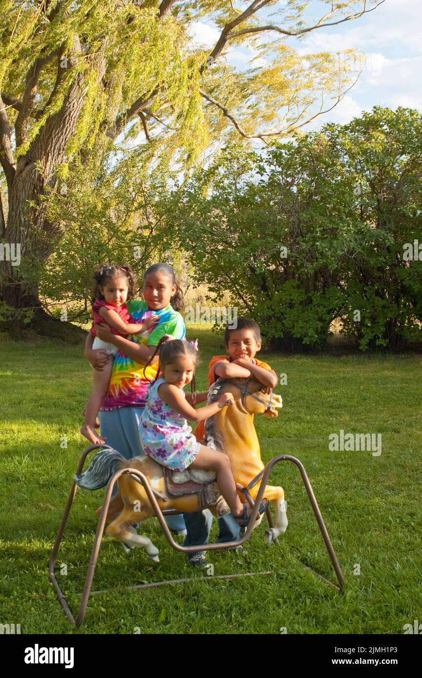 Children ranging in age from 1 to 12 years old who are cousins, sisters and brother. They play on a toy rocking horse in the backyard on the Fort Hall Stock Photo
