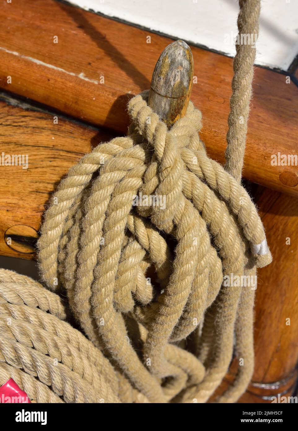 Rope coiled around traditional wooden cleat, peg, on sailing vessel Stock Photo