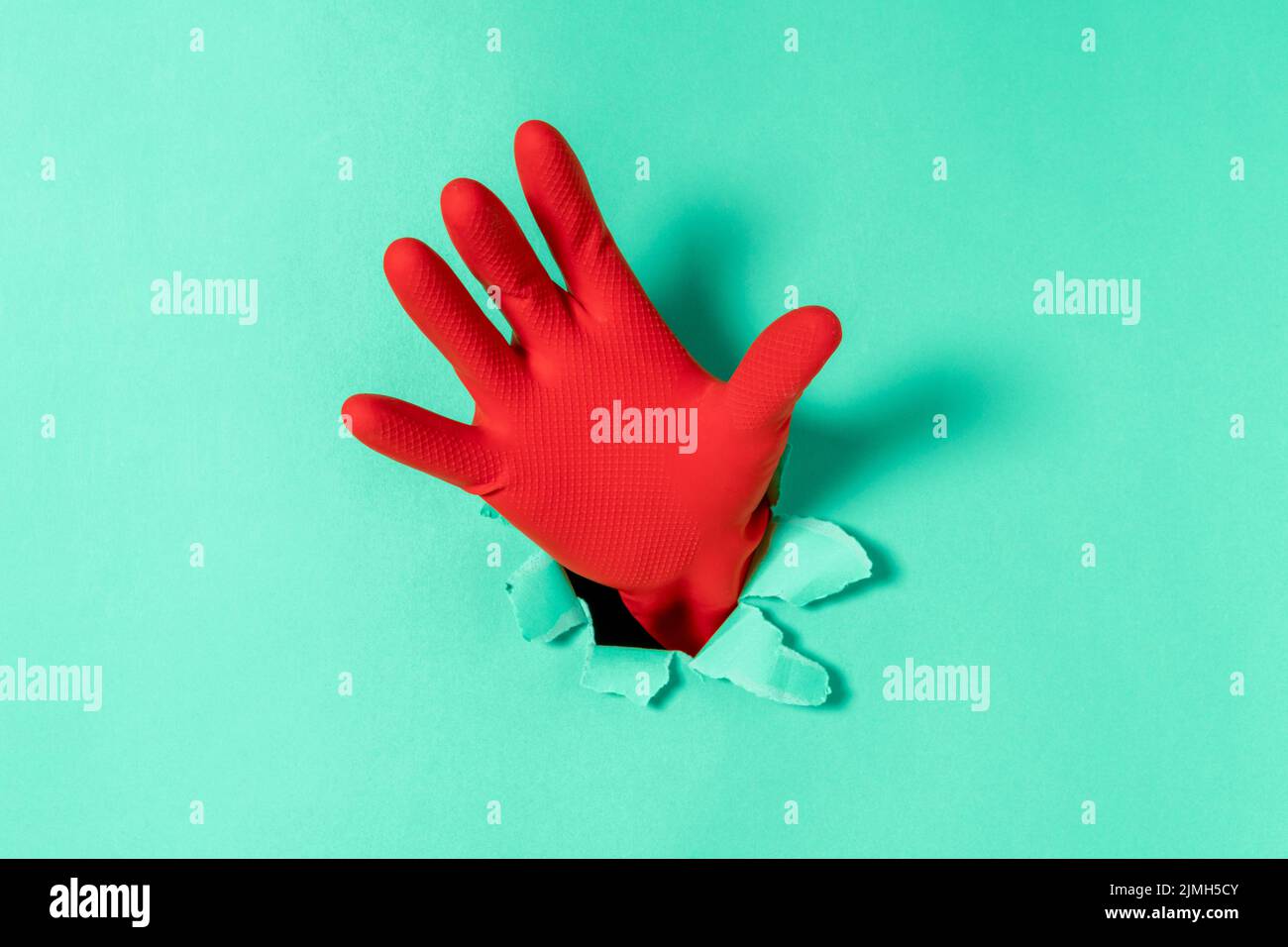 Hand in red glove sticks out of a torn hole in blue paper Stock Photo