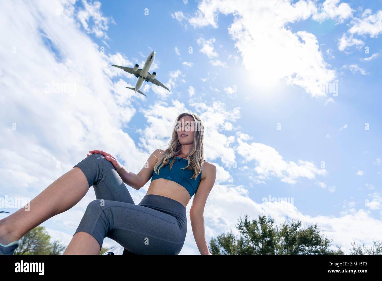 Lovely Blonde Female Traveler Enjoying The Summer Weather As A Commercial Aircraft Flies Overhead Stock Photo