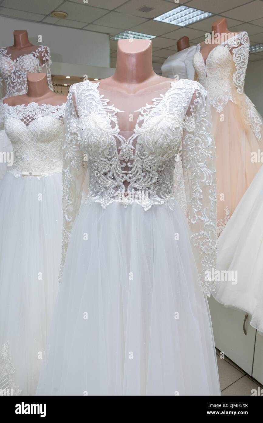 A beautiful white wedding dress on a mannequin. A close-up of a dress against other wedding dresses in a bridal shop. Stock Photo