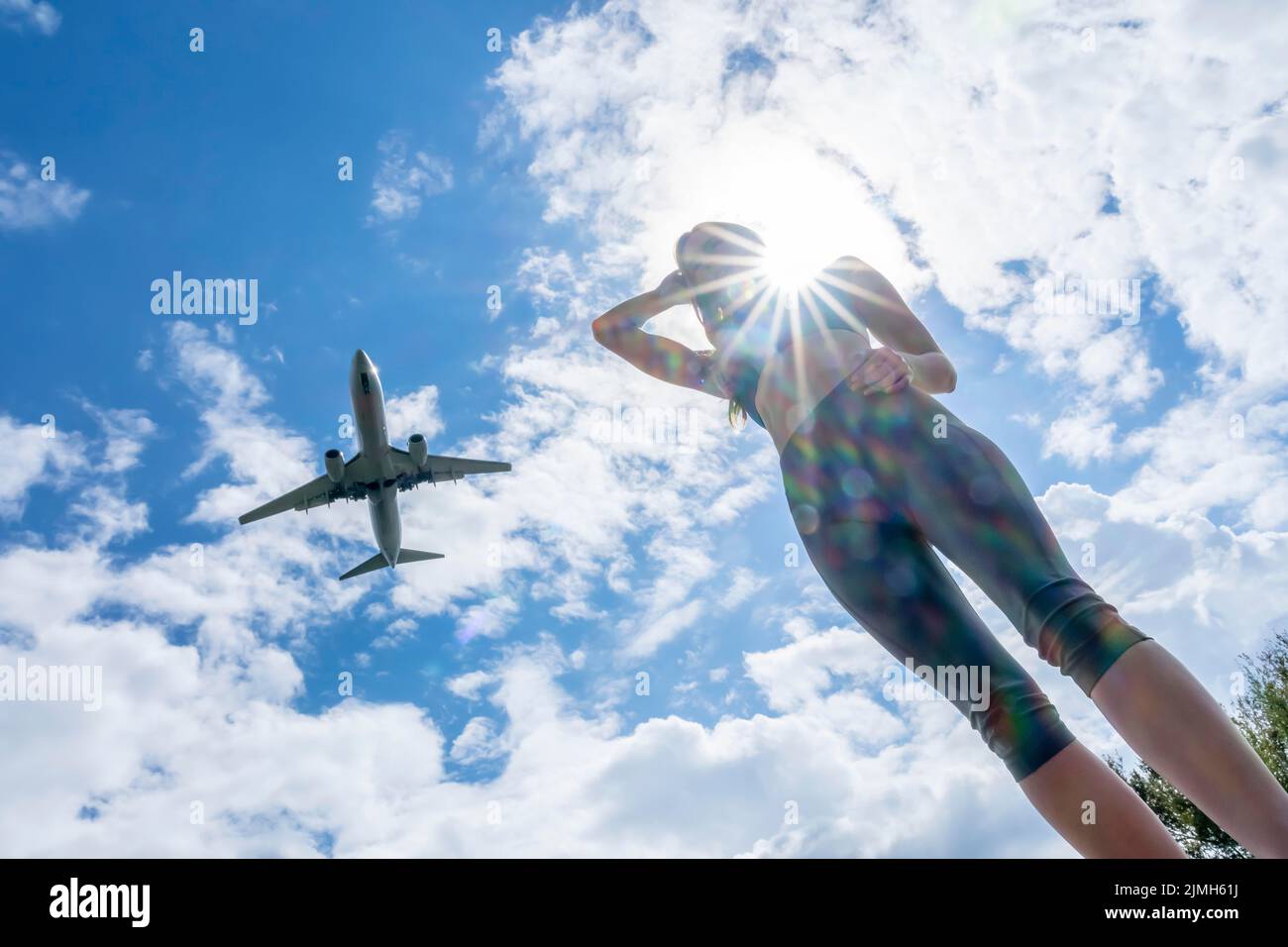 Lovely Blonde Female Traveler Enjoying The Summer Weather As A Commercial Aircraft Flies Overhead Stock Photo