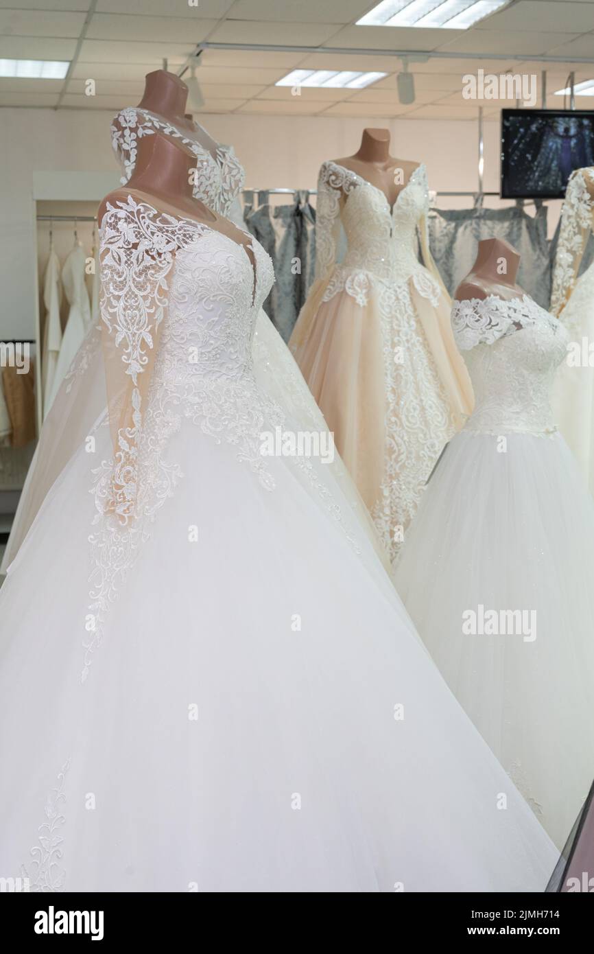 A beautiful white wedding dress on a mannequin. A wedding dress on the background of other wedding dresses in a wedding salon Stock Photo