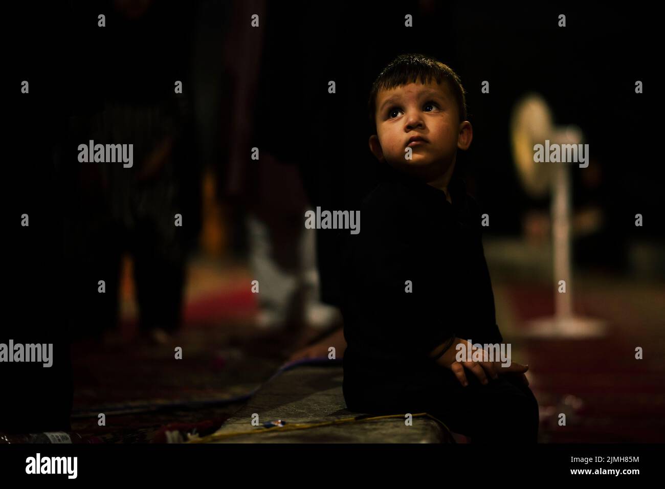 A Shia Muslim kid looks on during a religious procession on the 7th day of Muharram. Muharram is the first month of Islam. It is one of the holiest months on the Islamic calendar. Shia Muslims commemorate Muharram as a month of mourning in remembrance of the martyrdom of the Islamic Prophet Muhammad's grandson Imam Hussain, who was killed on Ashura (10th day of Muharram) in the battle of Karbala in 680 A.D. Stock Photo