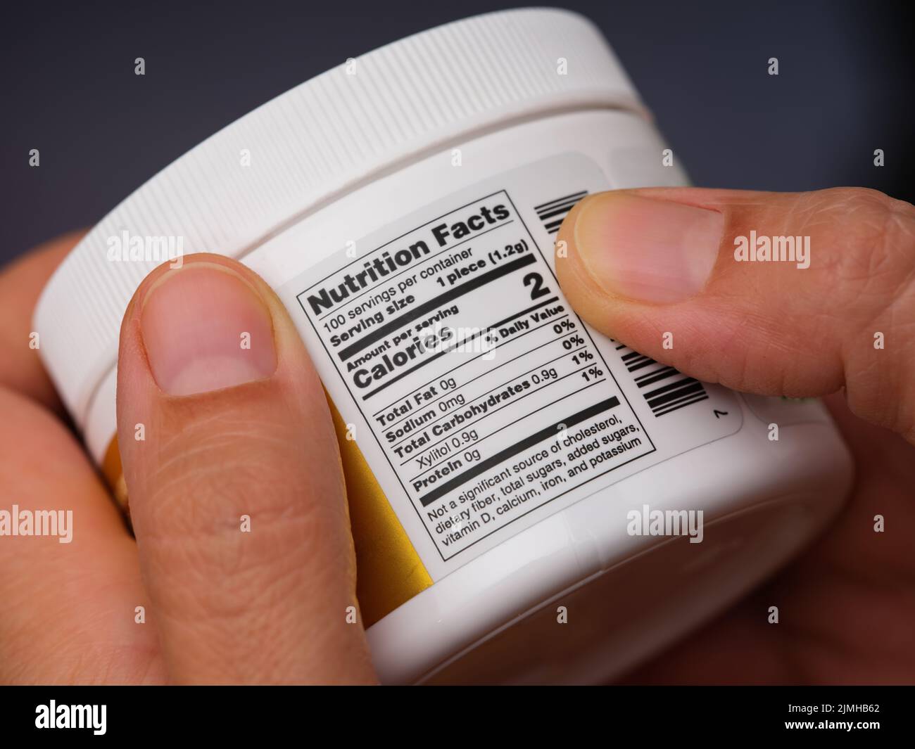 A woman holding a jar with gums and reading a Nutrition Facts label at the back. Stock Photo