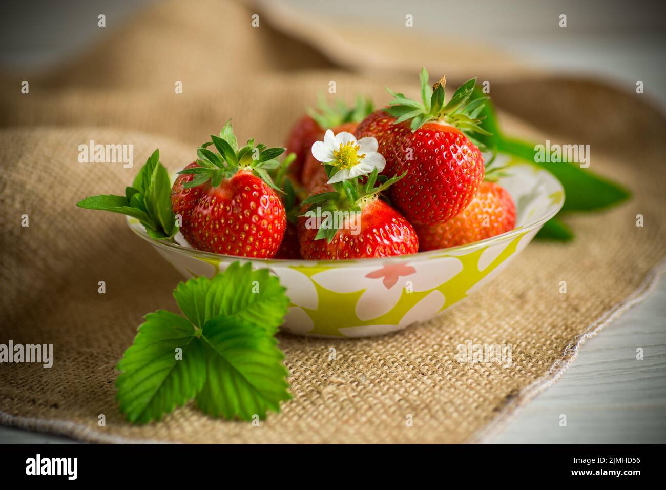 ripe red strawberries in a bowl on a burlap tablecloth, on a wooden table Stock Photo