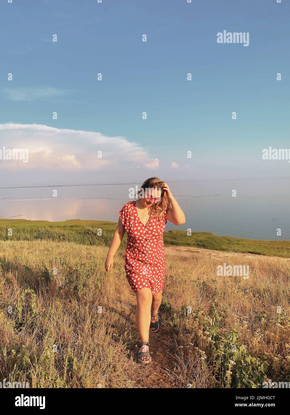 Happy woman in dress walking on country road along sea coast during summer vacation on sunny day Stock Photo