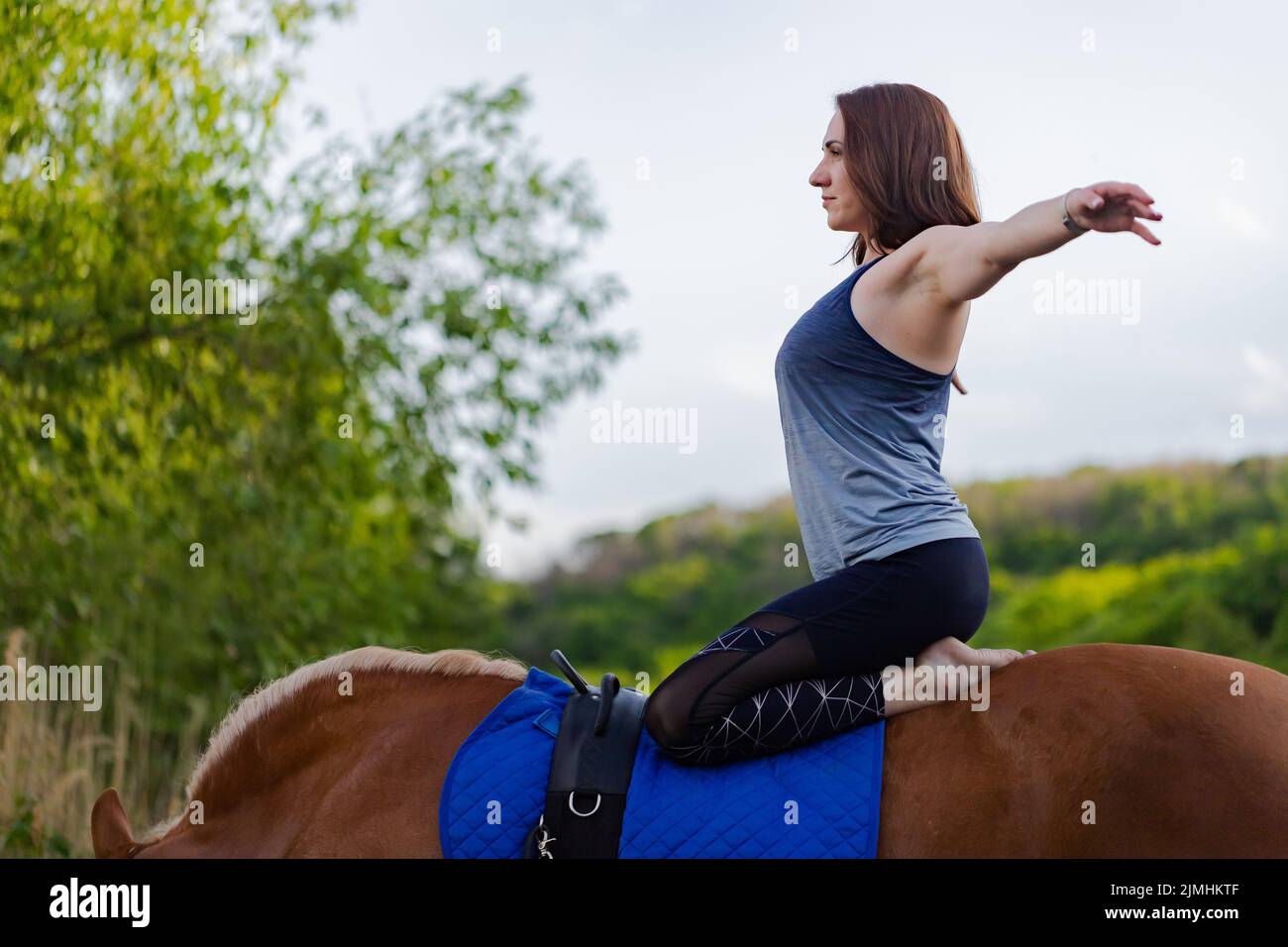 young woman doing yoga on a horse against the backdrop of trees Stock Photo