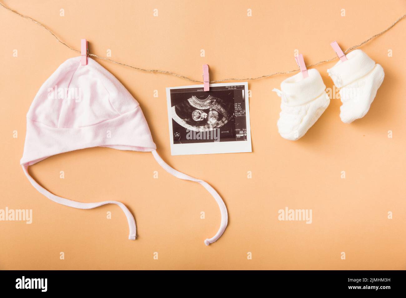 Baby s cap ultrasound picture pair woolen shoes hanging clothesline against orange backdrop Stock Photo