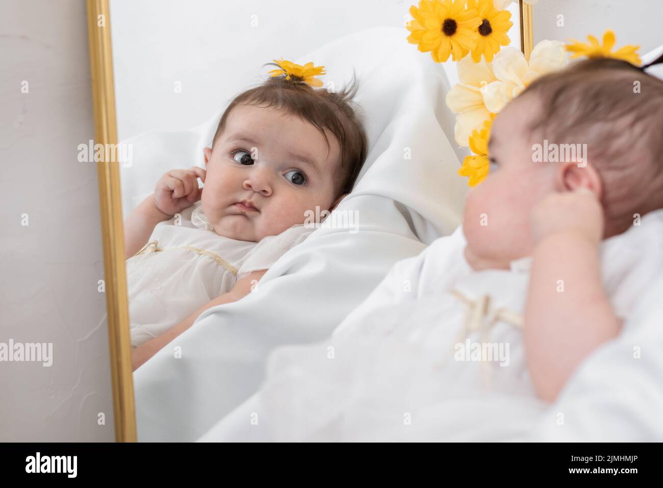 close-up of a beautiful latina baby girl, looking at her reflection in the mirror for the first time, touching her ear with her hand while looking ver Stock Photo