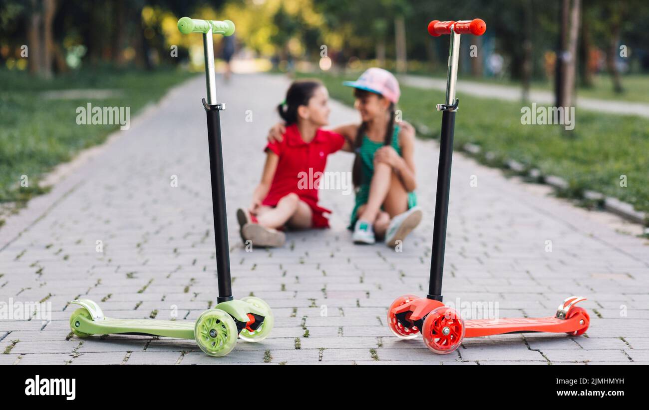 Push scooters front girls sitting walkway park Stock Photo Alamy