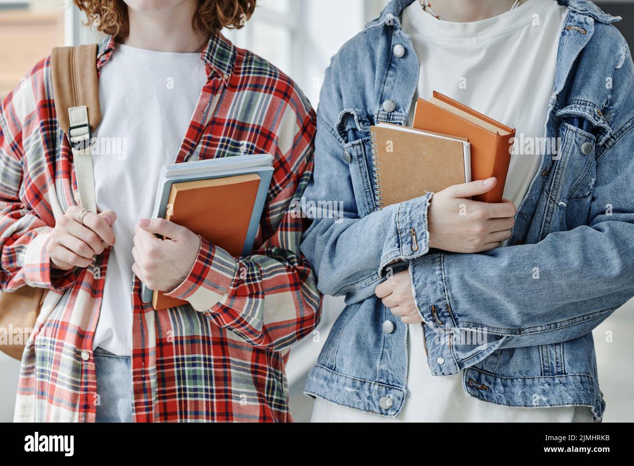 Close-up of two friendly teenage girls in casualwear holding books and copybooks by chest while standing in front of camera Stock Photo