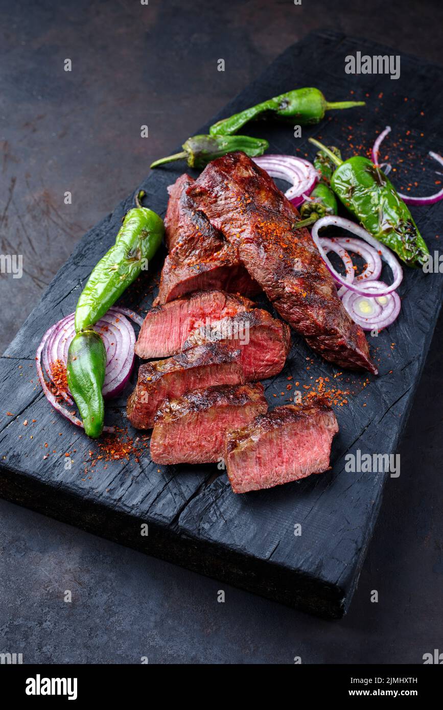 Traditional barbecue sirloin steak with chili and onion rings served as closeup on a charred