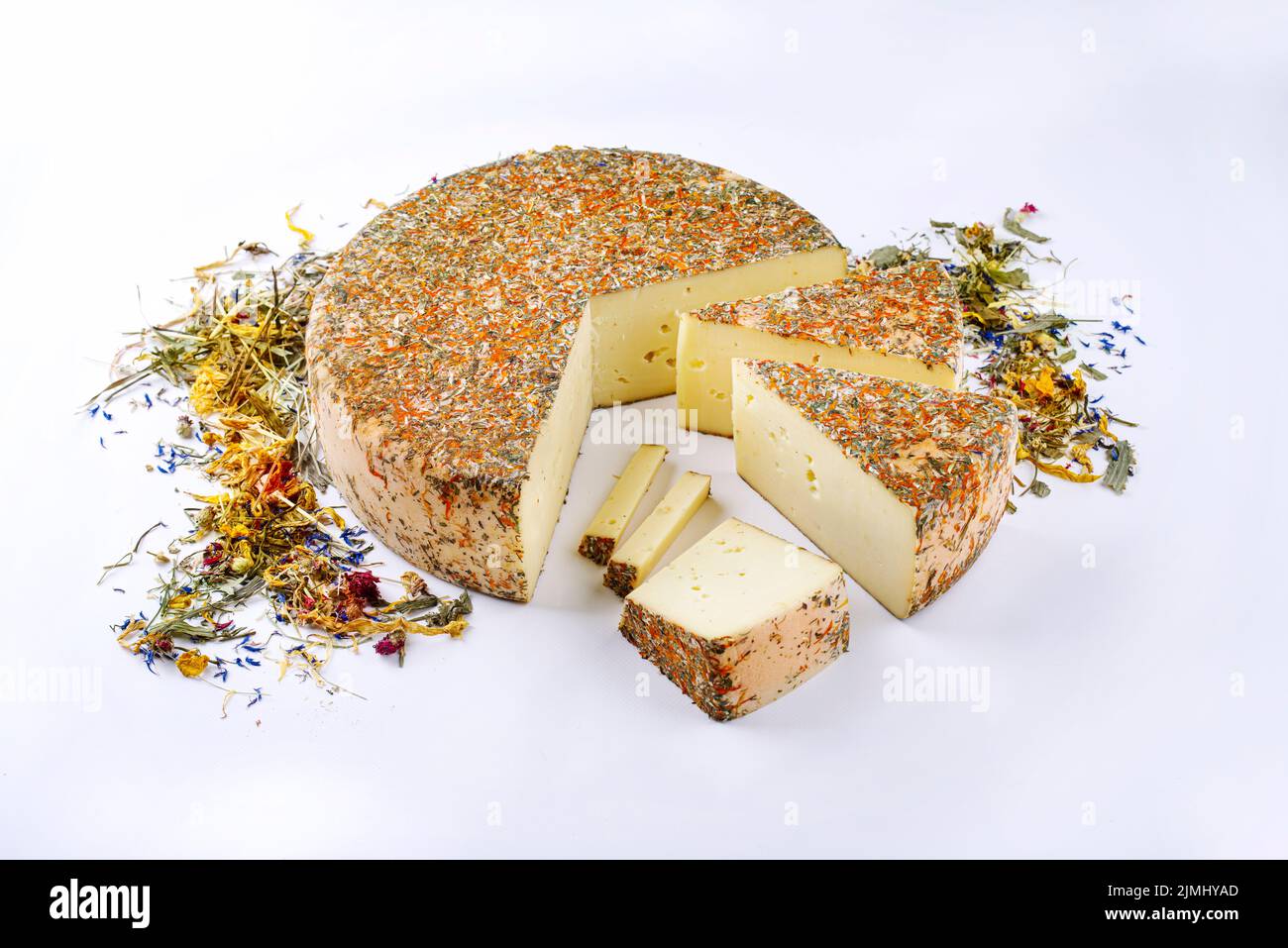 Traditional aged hay flower mountain cheese loaf of the Alps offered as loaf and sliced on white background with copy space Stock Photo