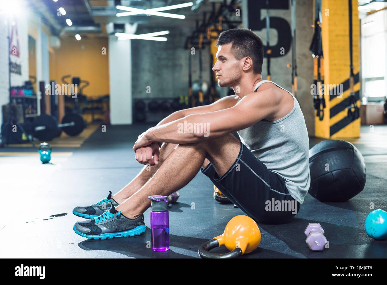 Side view young man sitting floor near exercise equipments water bottle Stock Photo