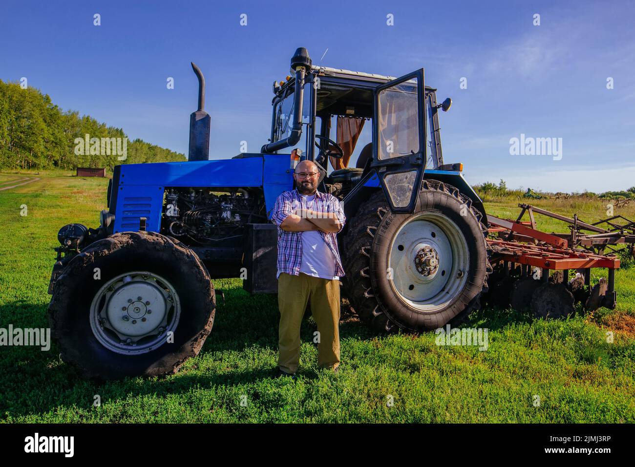 Farmer stands near the tractor on agricultural field Stock Photo