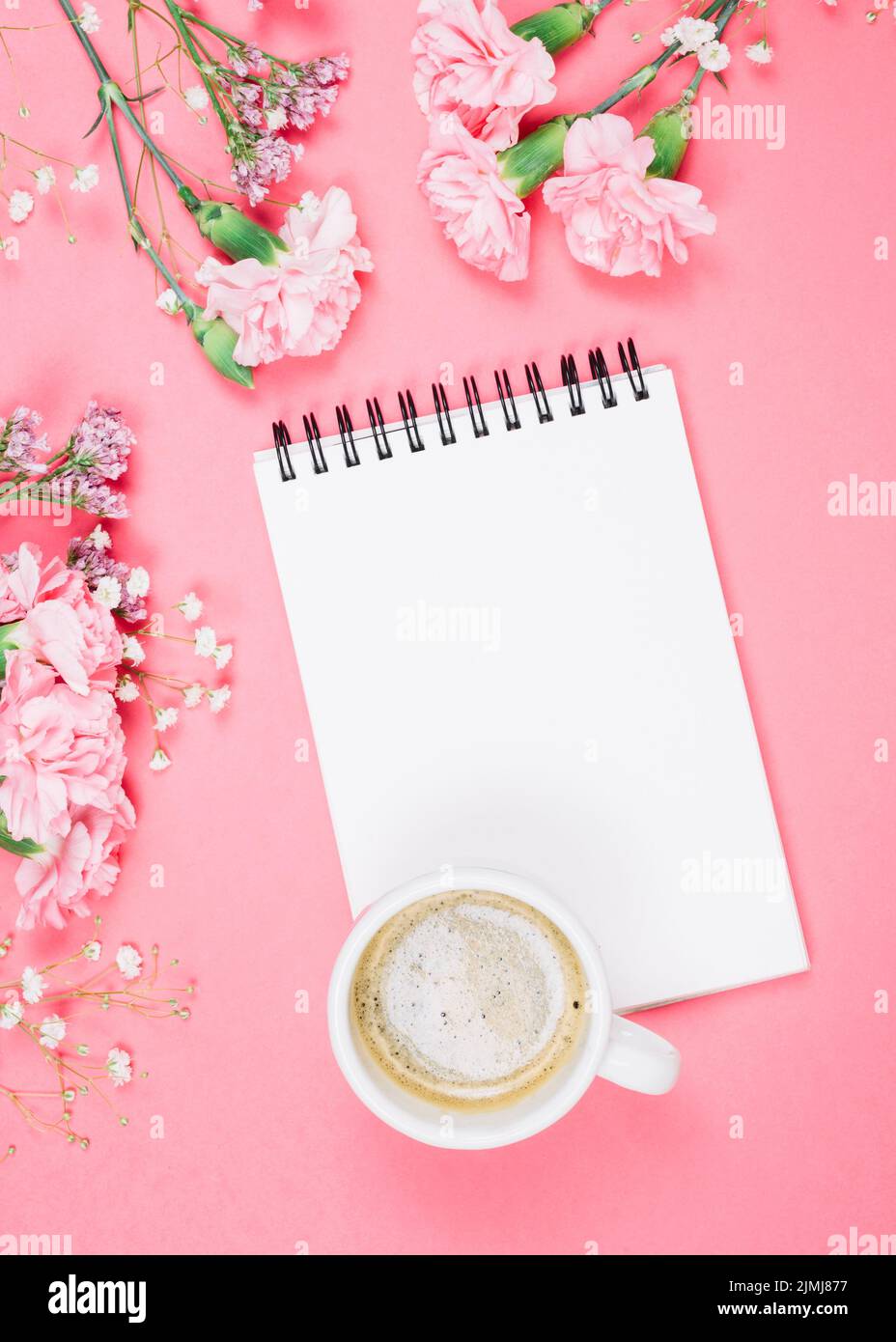 Overhead view coffee cup blank notepad with carnations gypsophila limonium flowers pink background Stock Photo
