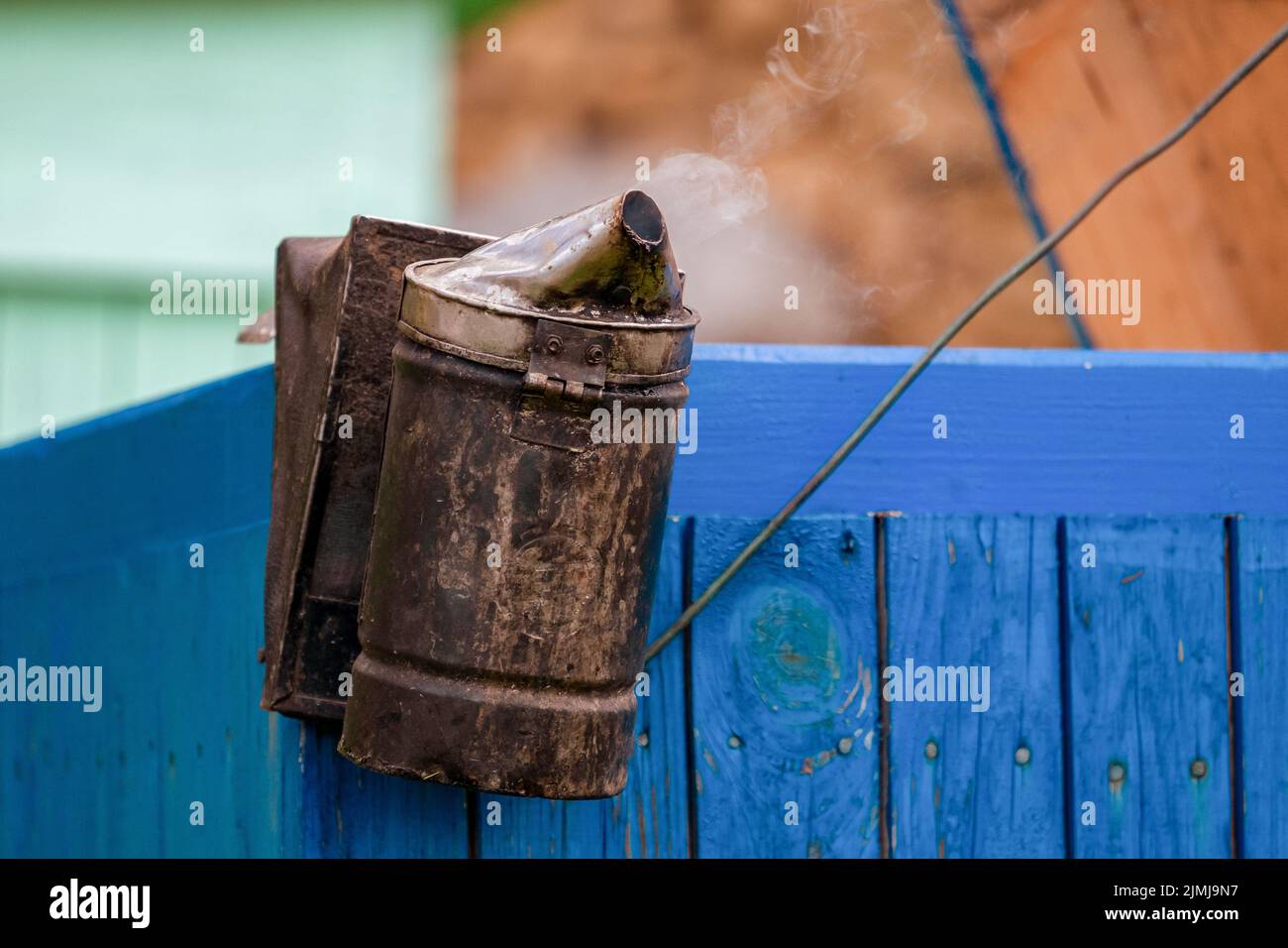 The beekeeper's smoker is working on the wall of the hive. Smoke billows Stock Photo