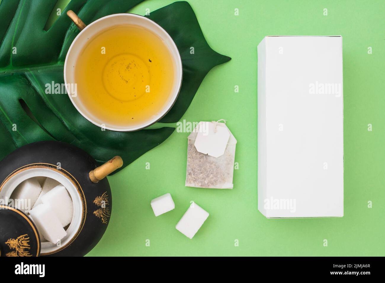 Overhead view herbal tea cup with sugar cubes tea bag box green background Stock Photo