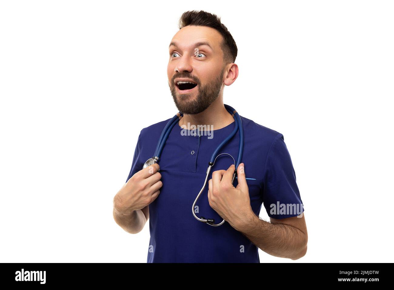 Dumbfounded doctor with a smile and an open mouth on the background of a white wall looks up to the left Stock Photo